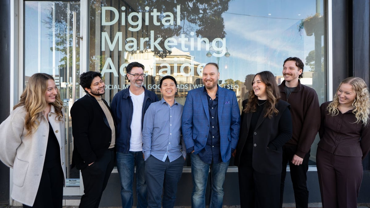 Group of eight professionals standing in front of a glass window displaying Digital Marketing text