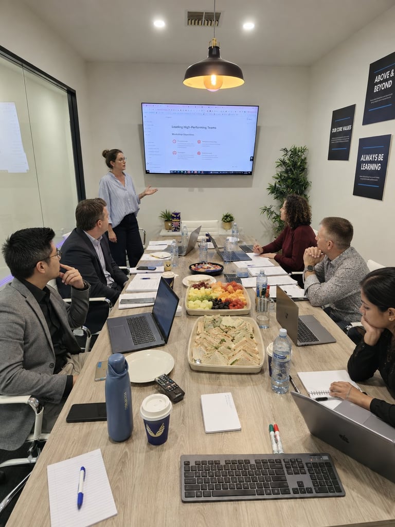Business team meeting in conference room with woman presenting at screen while colleagues sit at table with food and laptops