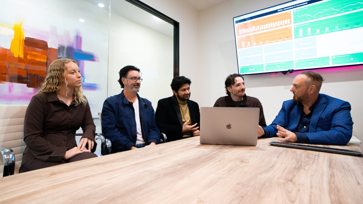 Five professionals meeting around a wooden table with a laptop and digital displays, planning where to focus SEO effort in 2026.