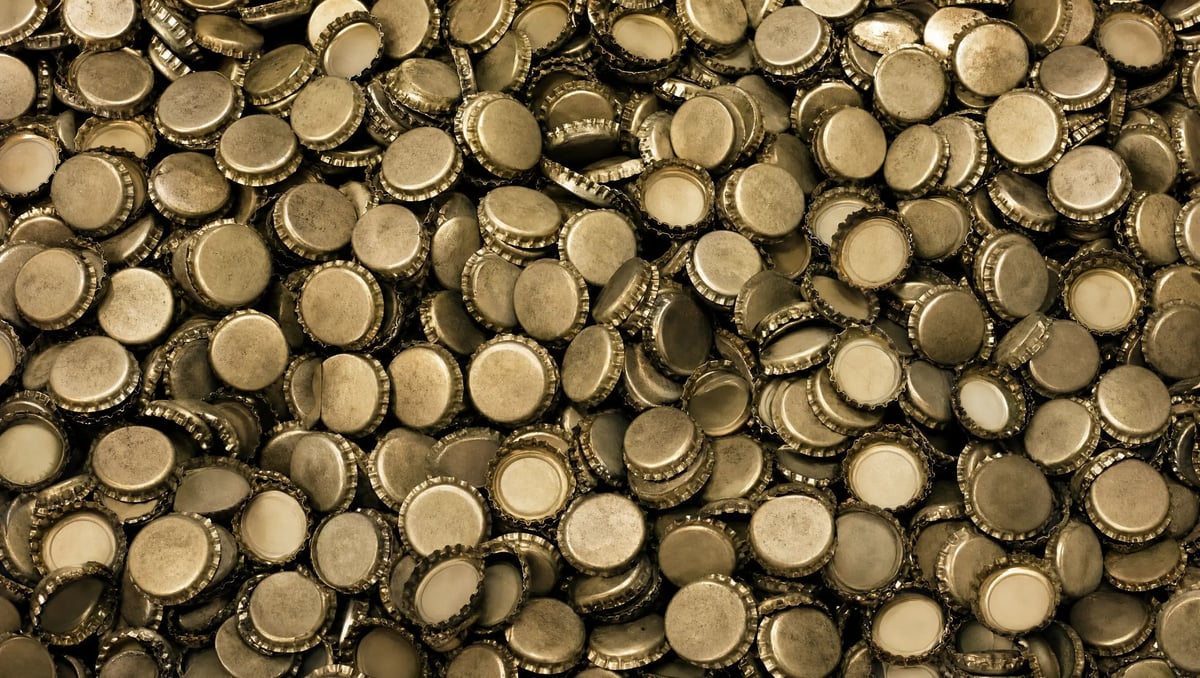 Close-up of numerous bottle caps with ridged metal edges and cream-colored centers scattered together